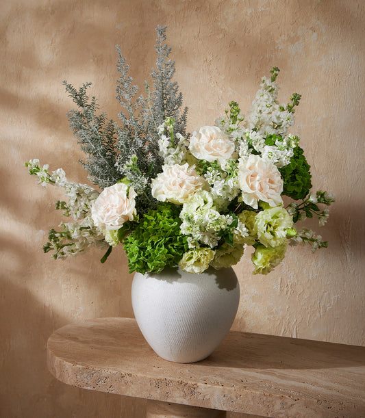 Elegant white ceramic vase with white and pink carnations, stock flowers, and green hydrangeas arrangement