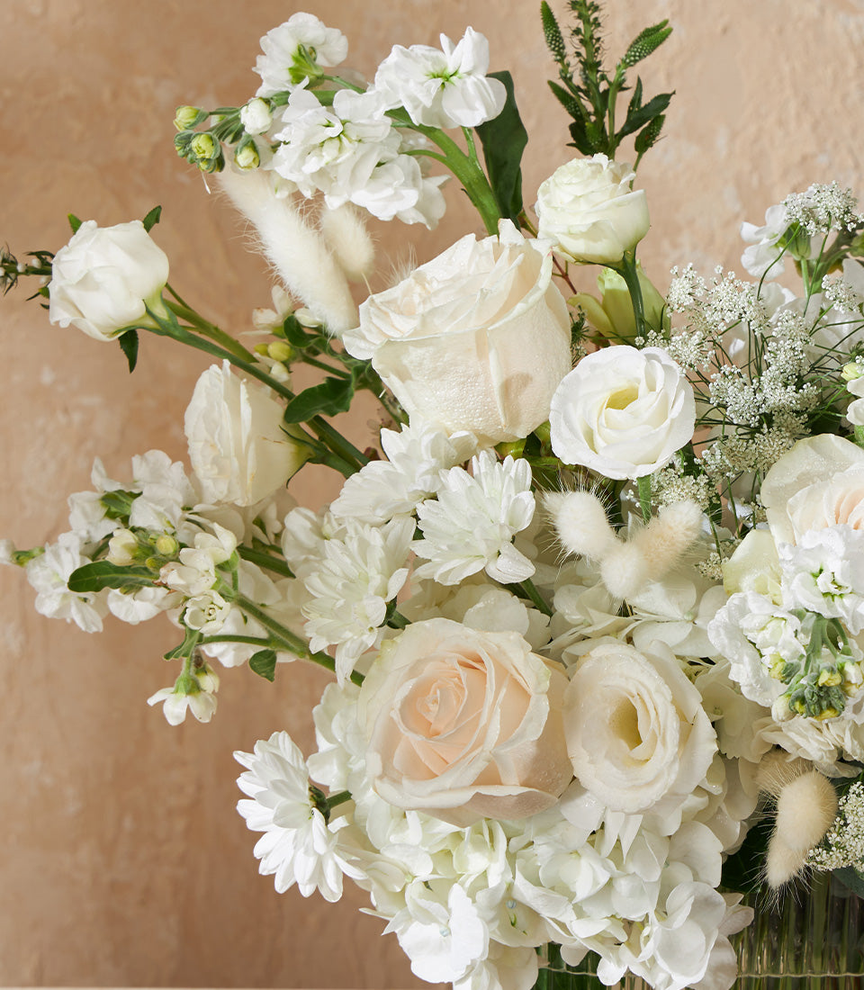 White roses and cream flowers in clear glass vase with baby's breath and bunny tail grass