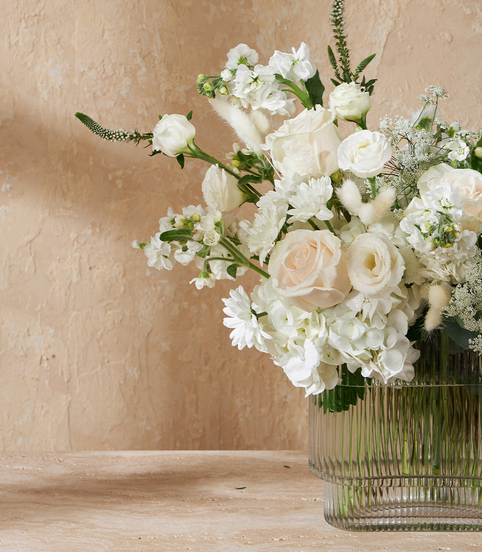 Lush white and light pink roses with hydrangeas in ribbed glass vase, elegant floral gift arrangement