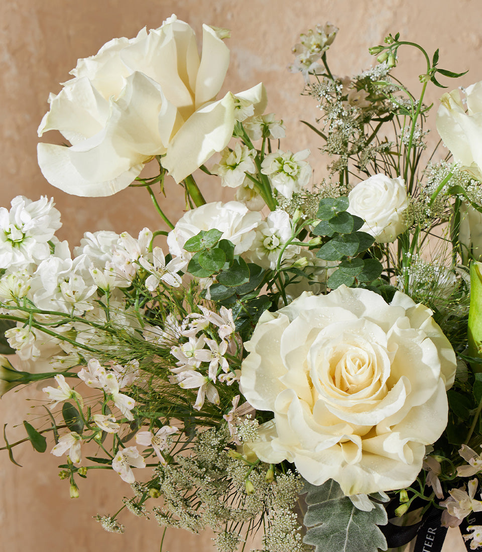 White and cream rose arrangement with stock flowers, eucalyptus, and greenery in elegant vase