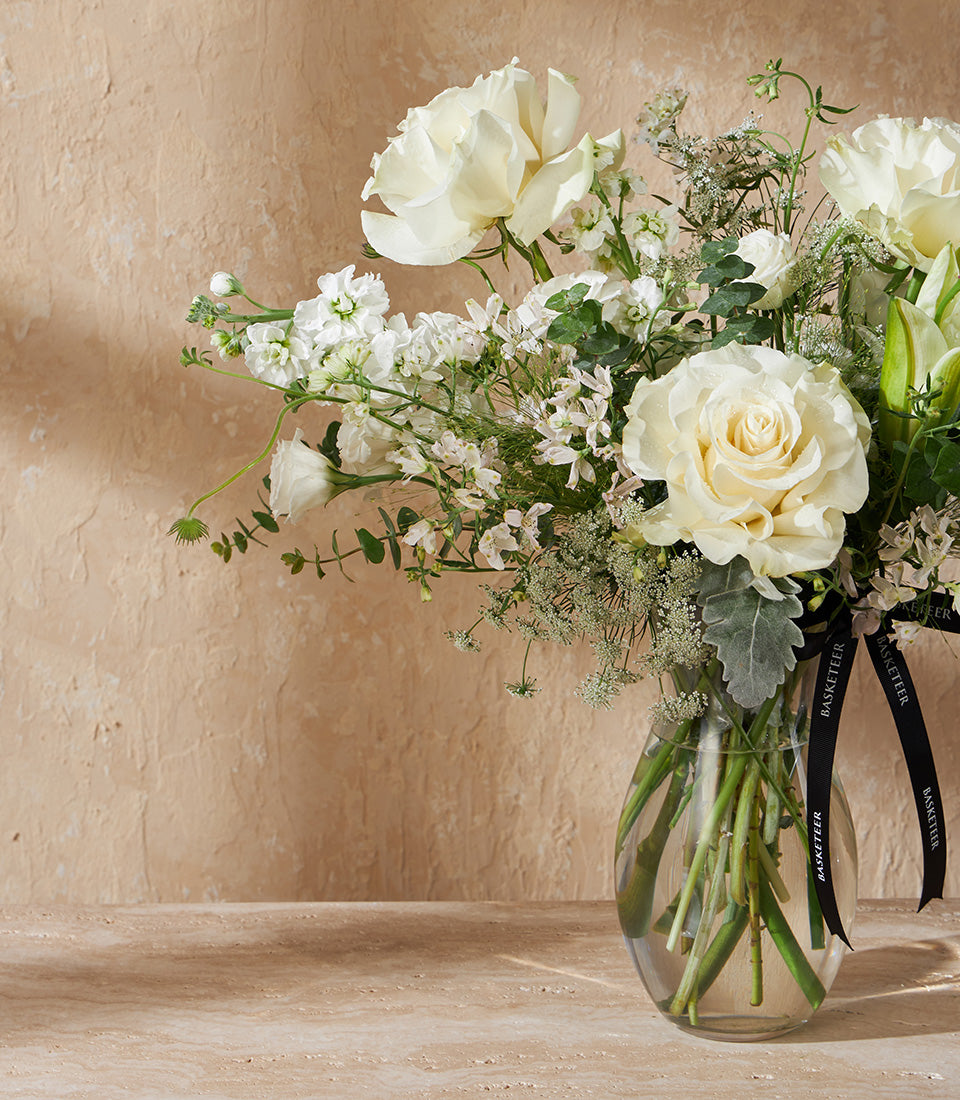White roses and stock flowers in clear glass vase with dusty miller greenery and black ribbon tie