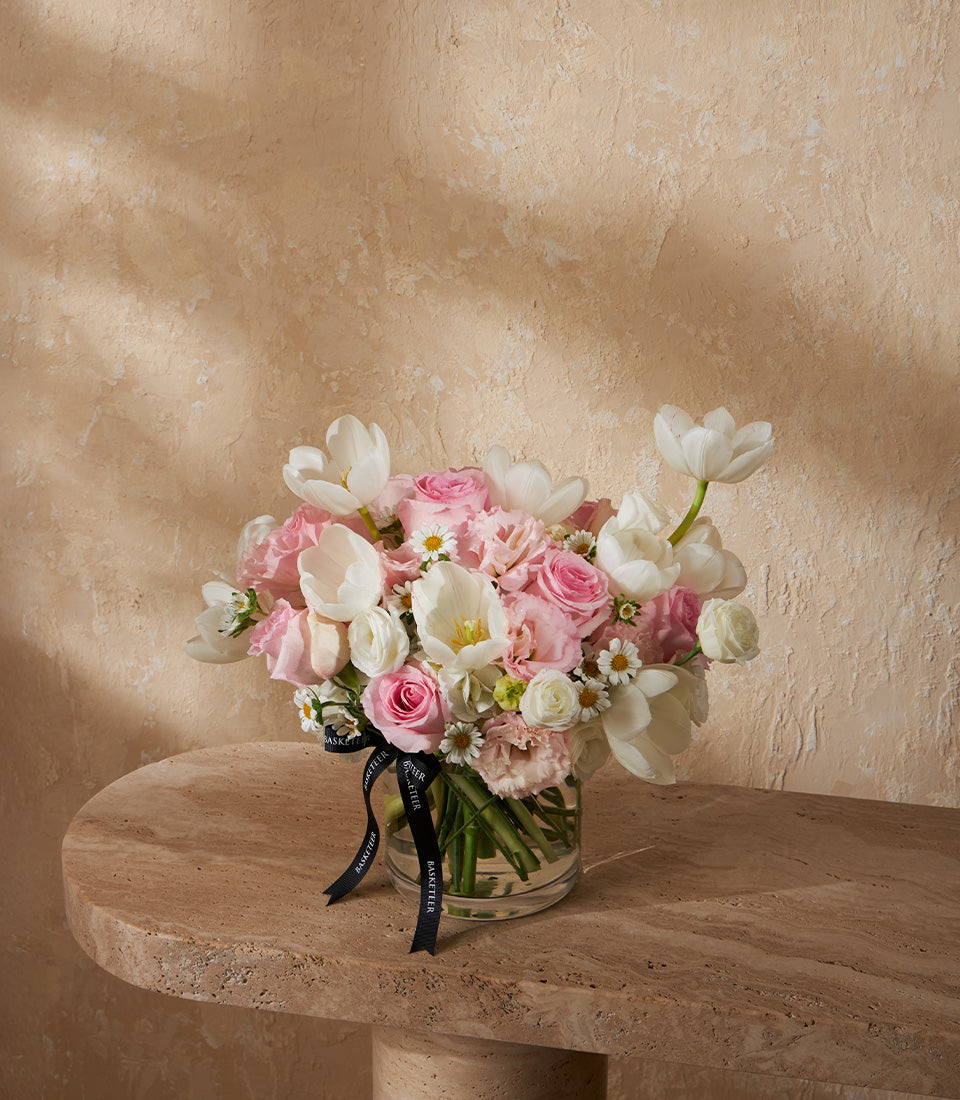 Graceful pastel vase arrangement with white tulips, pink roses, and white daisies in clear glass