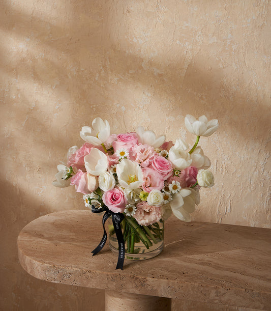 Graceful pastel vase arrangement with white tulips, pink roses, and white daisies in clear glass