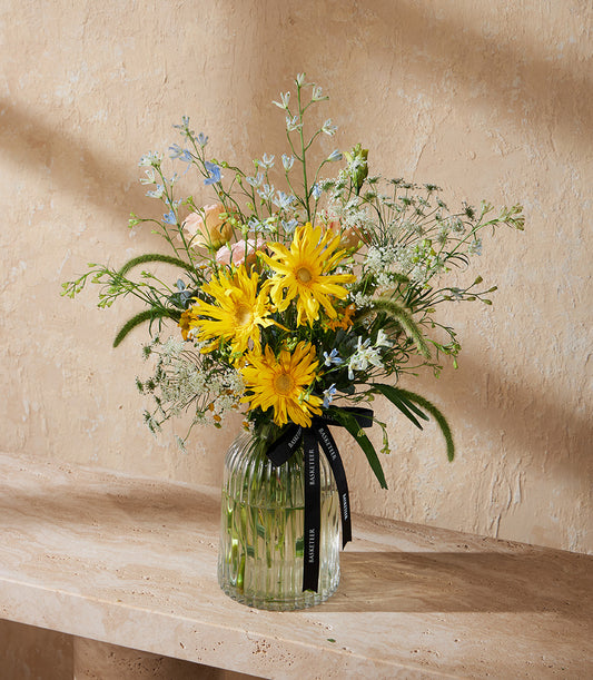Vibrant yellow daisy arrangement with white lace flowers and blue delphiniums in clear ribbed glass vase