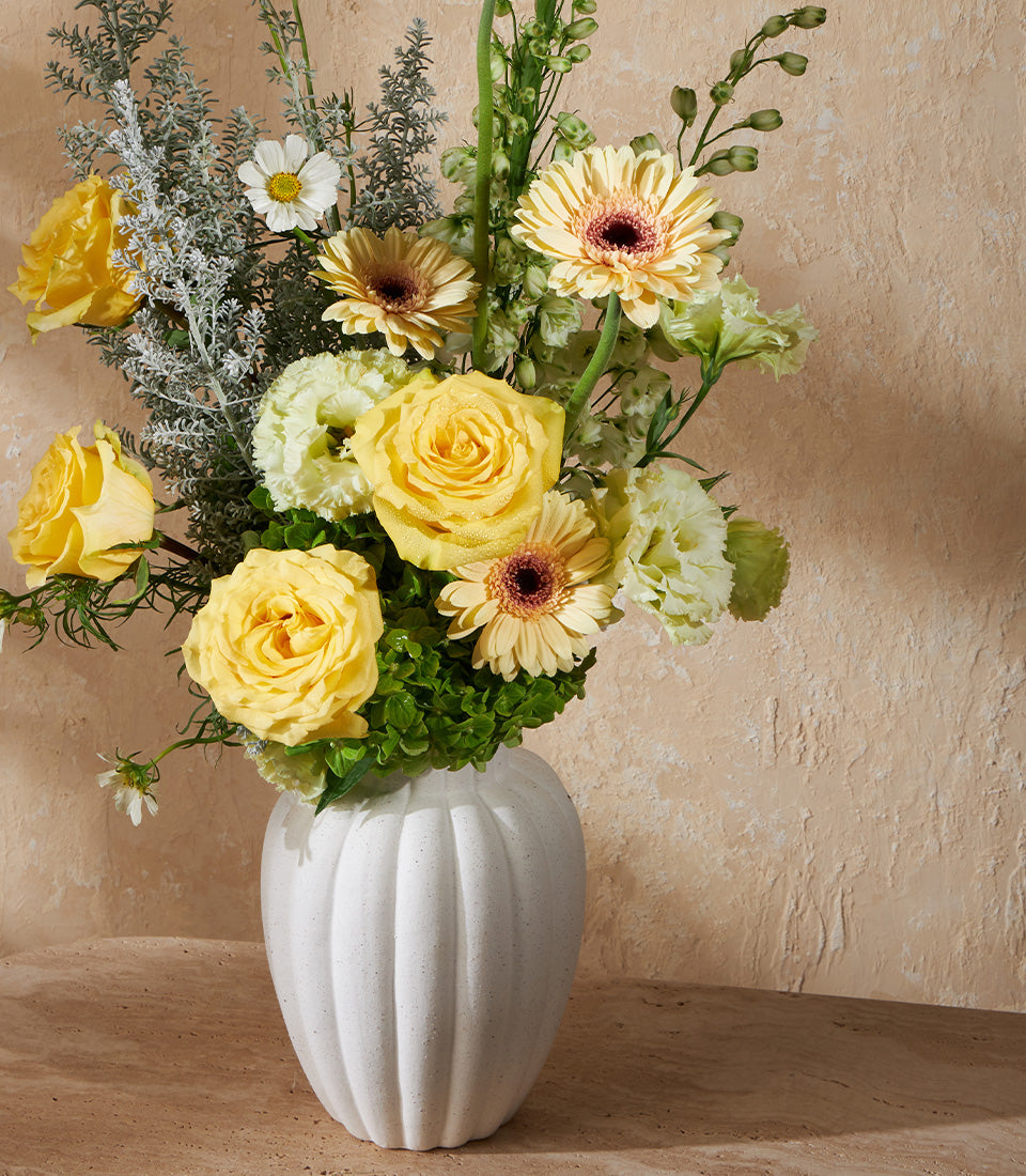 Yellow roses and gerbera daisies with green carnations in white ribbed vase