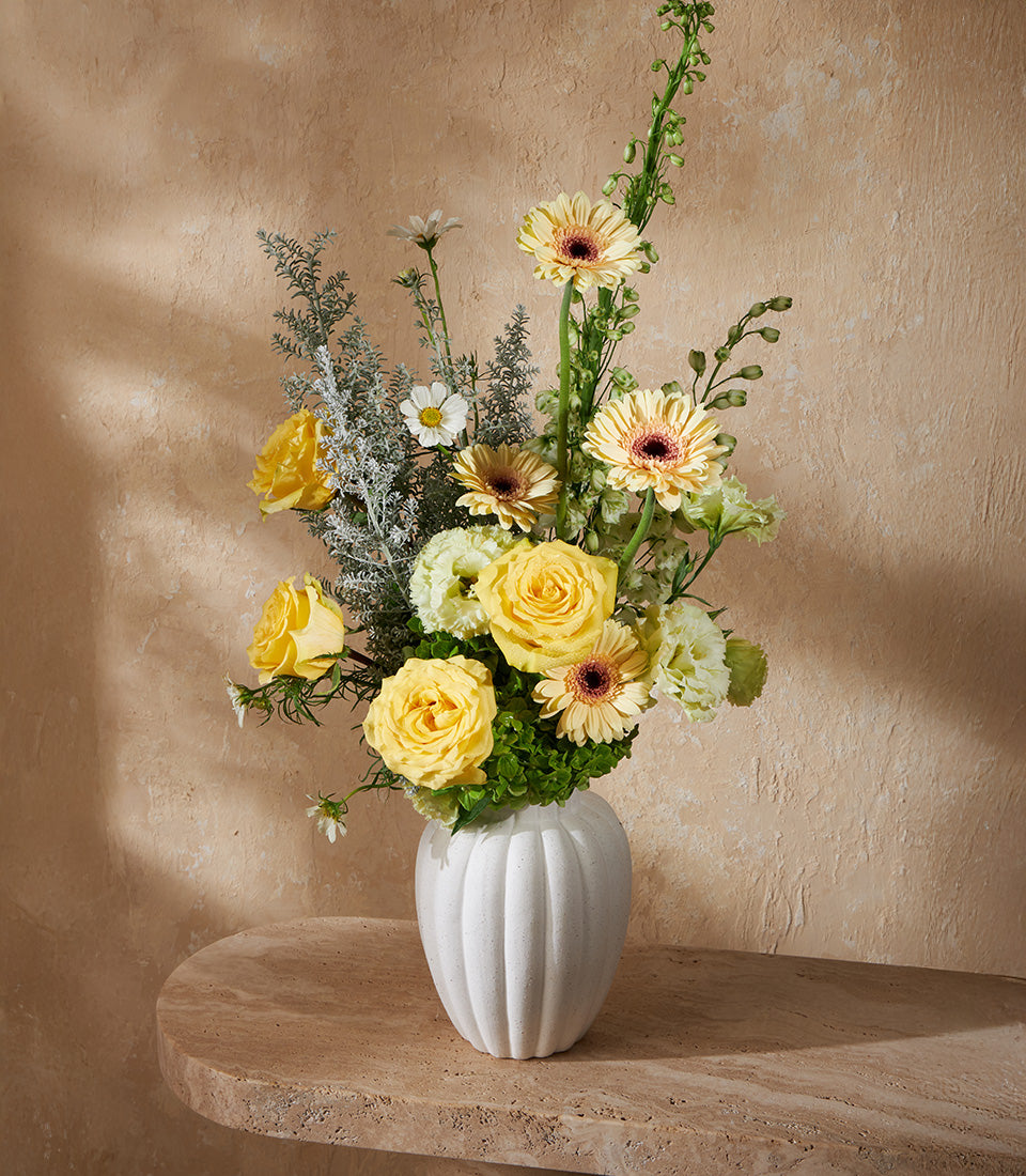 Yellow roses and gerbera daisies in white ribbed ceramic vase with lisianthus and dusty miller