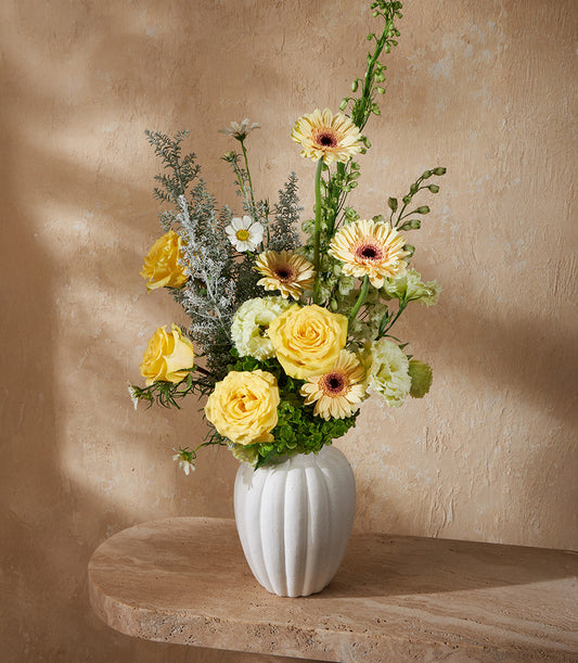Yellow roses and gerbera daisies in white ribbed ceramic vase with lisianthus and dusty miller