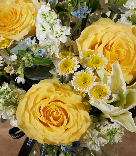 Golden yellow roses and white daisies in clear glass vase with black ribbon detail