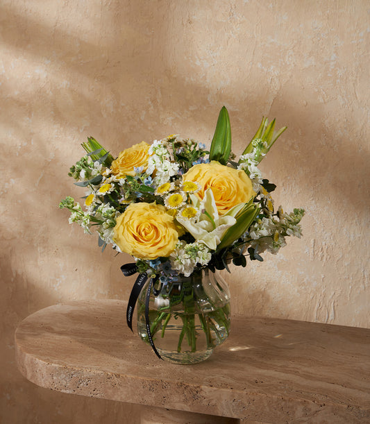 Vibrant yellow roses and white lilies in a clear glass vase with luxury gift ribbon