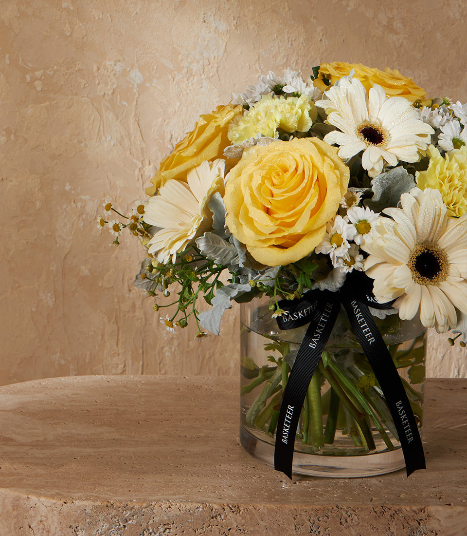 Yellow and white rose arrangement in clear glass vase with Basketeer signature black ribbon