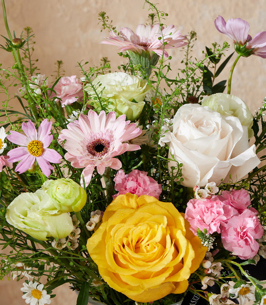 Vibrant spring flower arrangement with yellow and white roses, pink gerberas, and green ranunculus in lush mixed bouquet