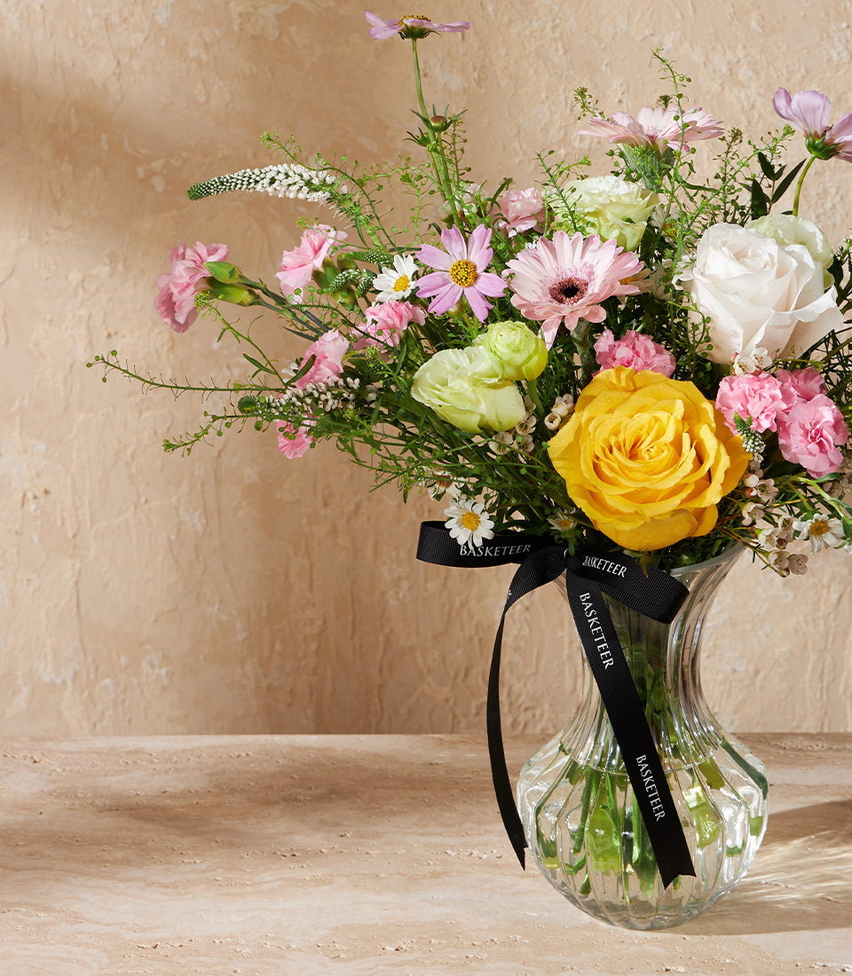Vibrant mixed flower arrangement with yellow and white roses, pink gerberas and carnations in ribbed glass vase with black