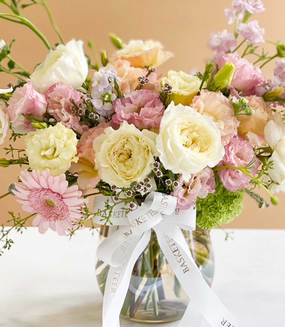 Bright pastel flower arrangement with roses, lisianthus, and gerbera in clear glass vase