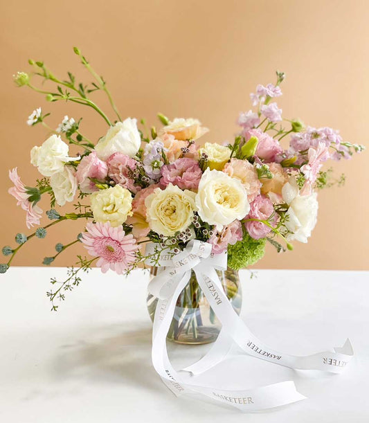 Vibrant mixed flower arrangement with roses and lisianthus in white, cream, pink, and purple tones in clear glass vase