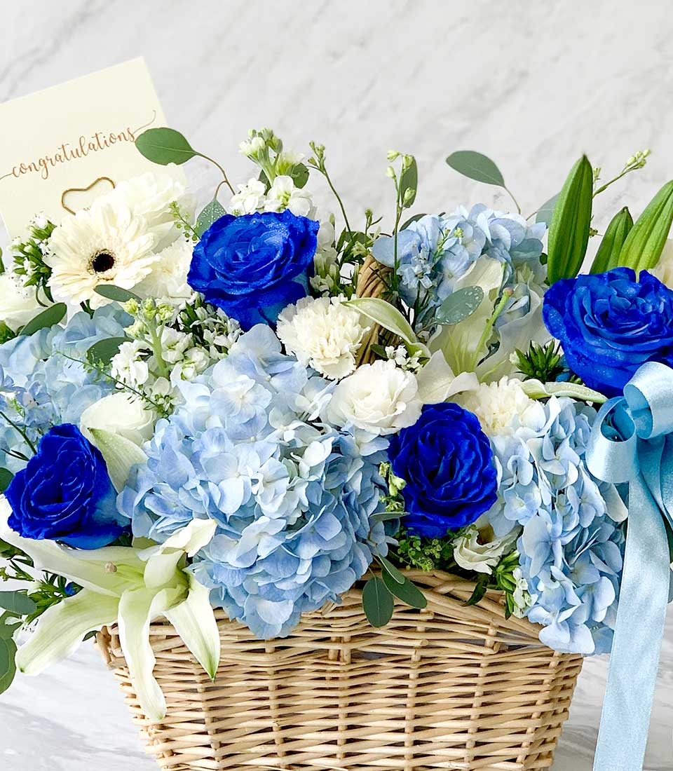 Blue and white fresh flower basket with royal roses, hydrangeas, lilies, and gerberas in wicker