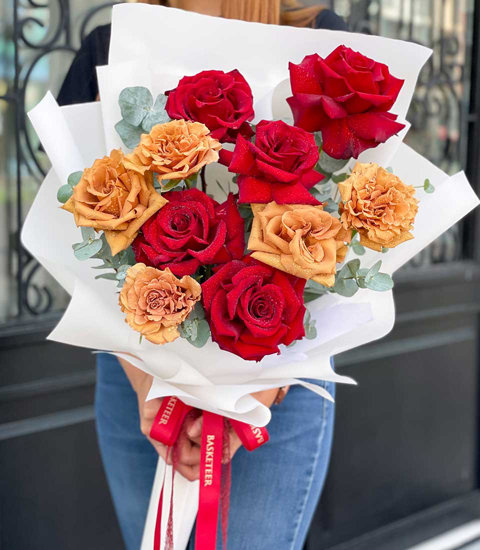Fresh red and orange rose bouquet with eucalyptus wrapped in white paper and red ribbon
