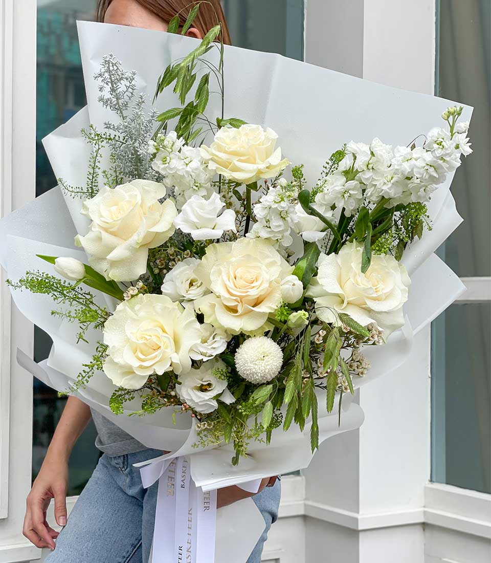 Elegant white rose and tulip graduation bouquet with cream stock flowers and fresh greenery, wrapped in white paper