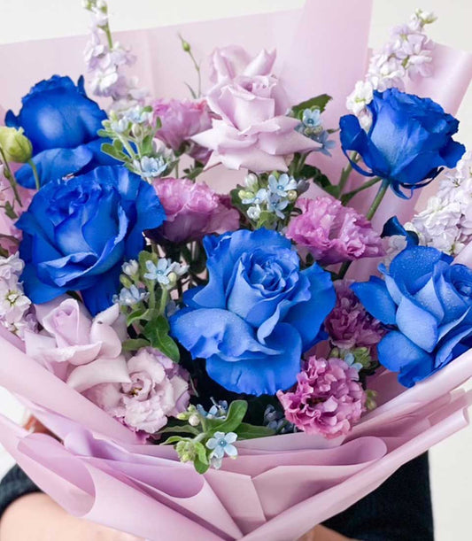 Vibrant blue and purple rose bouquet with lavender accents and delicate forget-me-nots, wrapped in soft pink paper