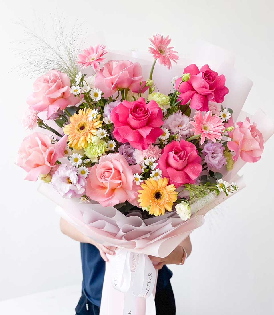 Vibrant pink and yellow fresh flower bouquet with roses and gerbera daisies, wrapped in light pink paper with white ribbon