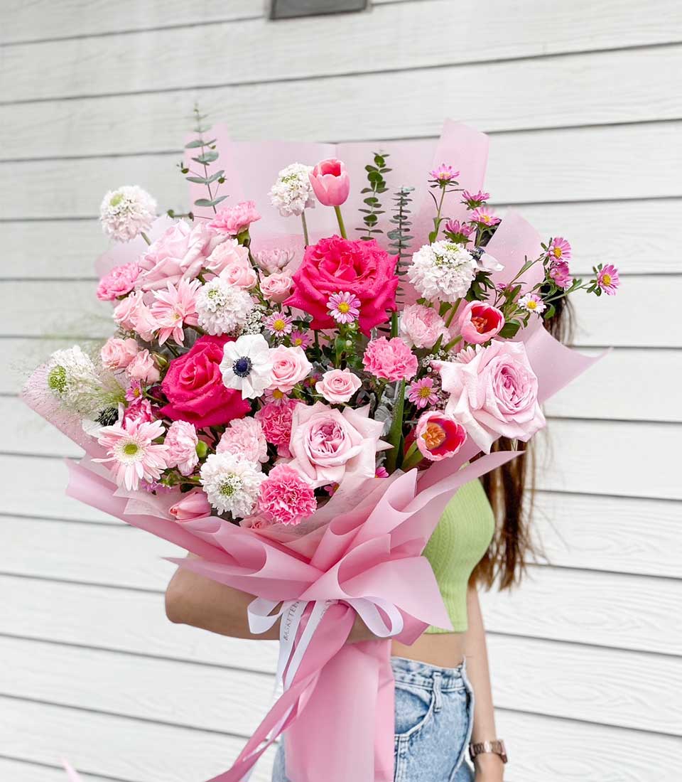 Fresh pink roses, carnations, and tulips bouquet with white anemones and eucalyptus, wrapped in pink paper