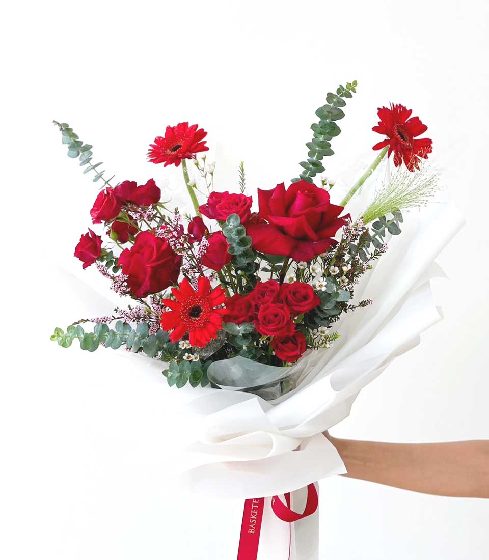 Vibrant red roses and gerbera daisies graduation bouquet with eucalyptus, hand-held in white paper wrap