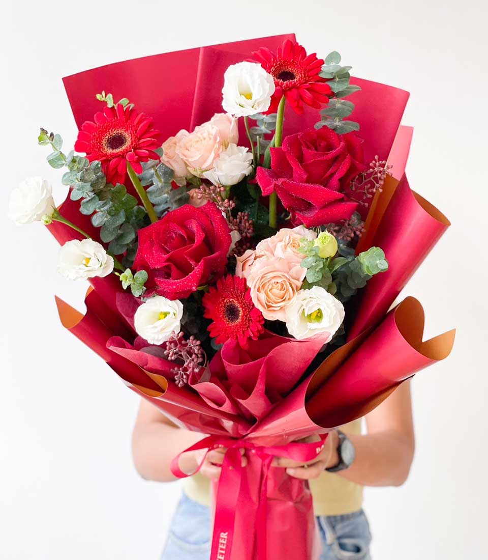 Vibrant red roses and gerbera daisies graduation bouquet with white lisianthus and eucalyptus, wrapped in red paper