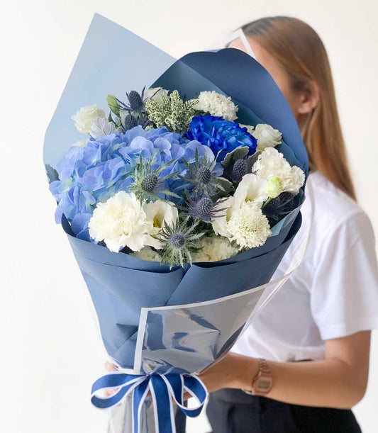 Vibrant blue hydrangea graduation bouquet with white carnations and thistles, navy wrapped