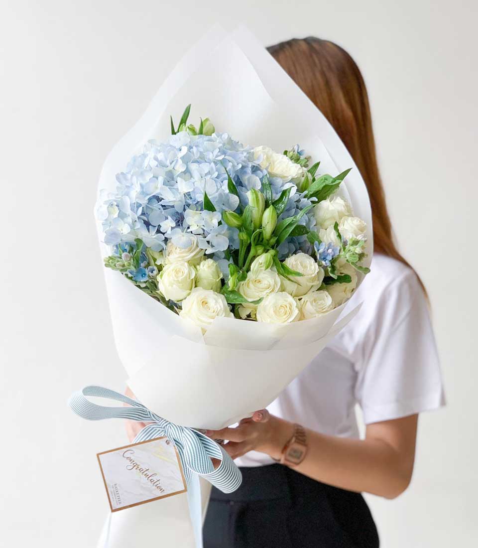 Light blue hydrangea bouquet with white roses and green foliage, tied with blue striped ribbon