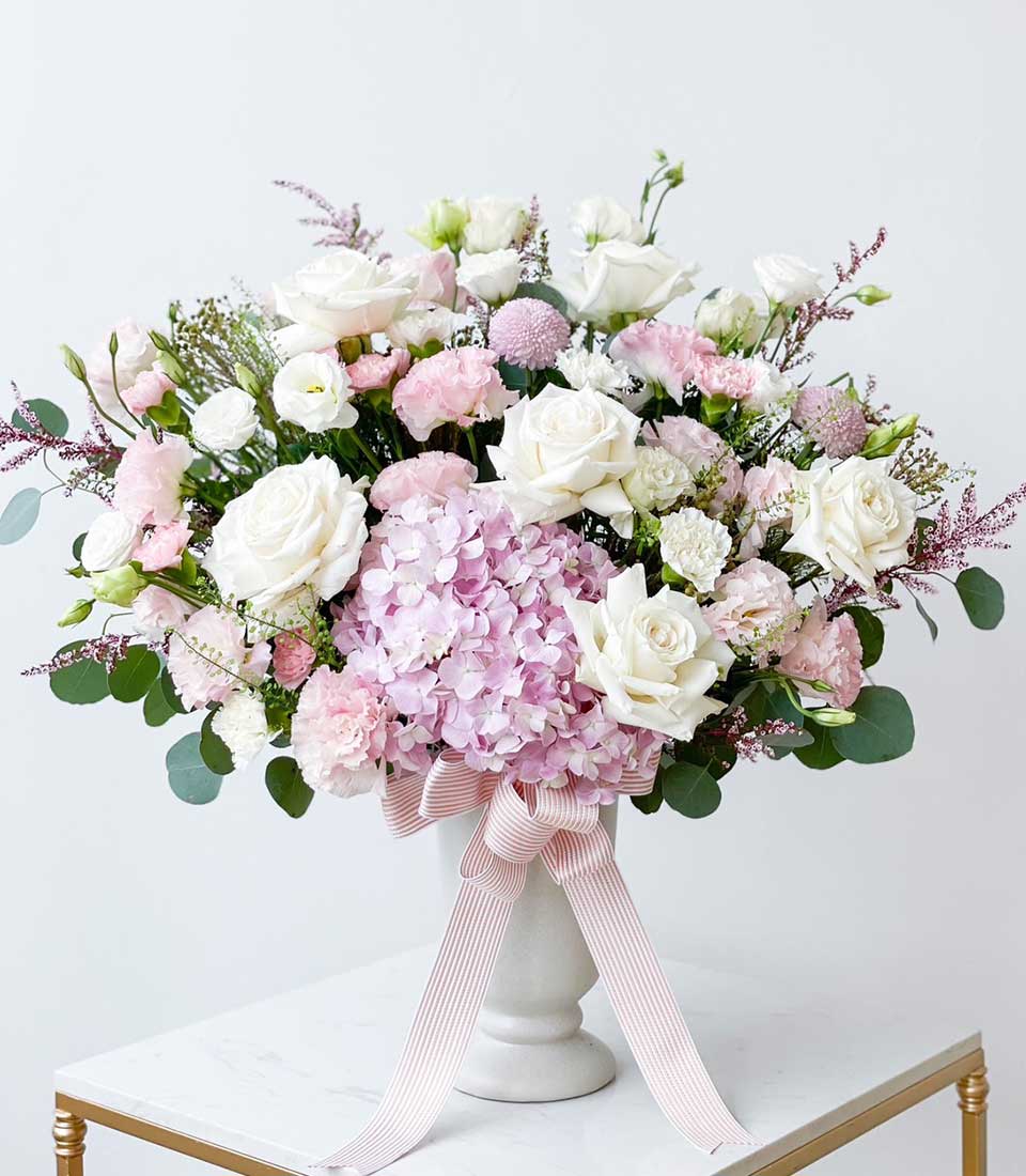 Blush Serenity white ceramic vase with white roses, pink hydrangeas, and eucalyptus greenery, tied with pink-striped ribbon