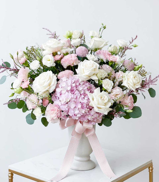 Blush Serenity white ceramic vase with white roses, pink hydrangeas, and eucalyptus greenery, tied with pink-striped ribbon