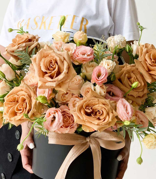 Radiant toffee roses and peach blooms in luxury black hatbox with beige ribbon bow