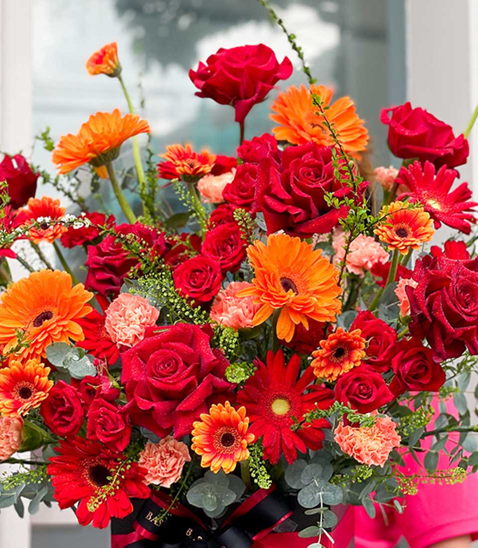 Vibrant scarlet and orange rose bouquet with gerbera daisies, fresh birthday flowers in dark box