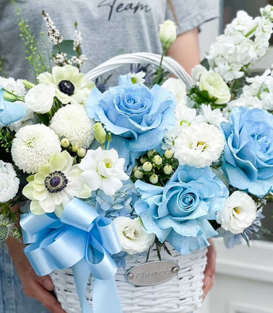 Blue and white rose arrangement in white woven basket with satin ribbon bow, premium fresh flowers