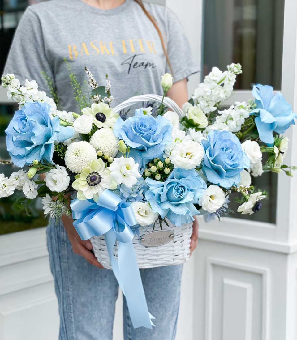 Blue and white roses with anemones in white woven gift basket, light blue satin ribbon