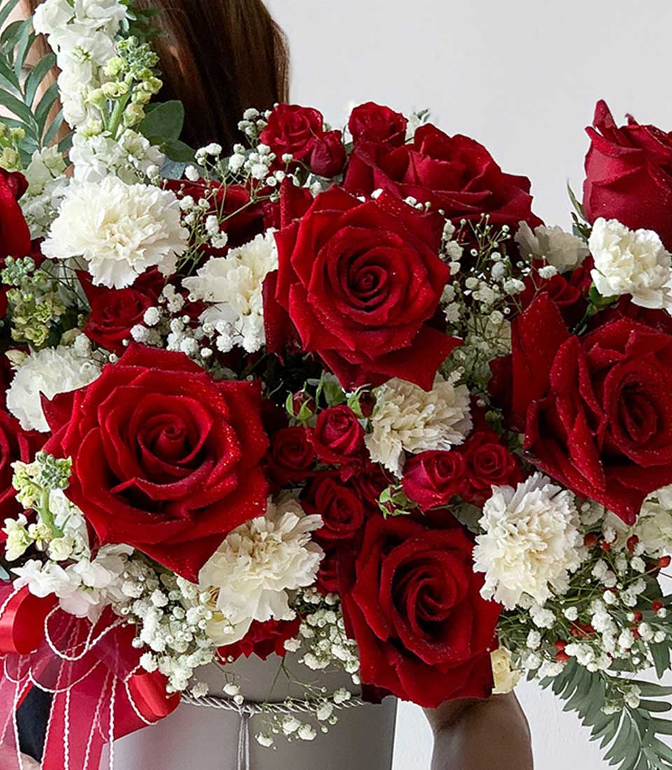 Red roses and white carnations graduation flower arrangement in grey hatbox with ribbon