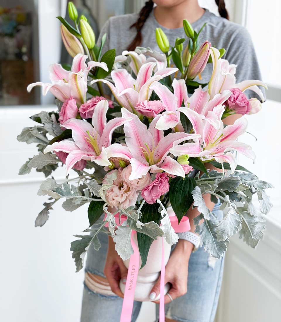Elegant pink lily and rose bouquet in white vase with dusty miller and green foliage, perfect for birthdays and celebrations
