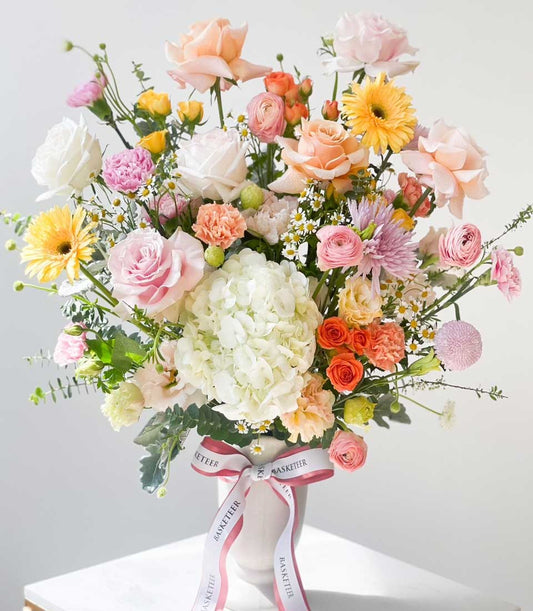 Vibrant mixed flower arrangement in white vase with roses, hydrangeas, and daisies
