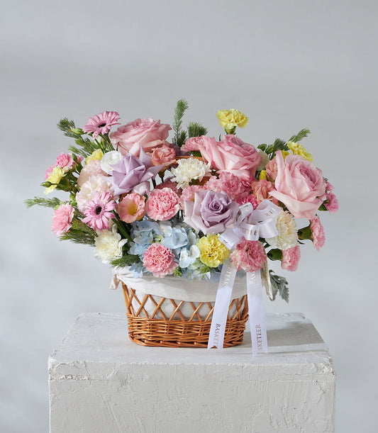 Vibrant pastel flower basket with pink roses, hydrangeas, and daisies in woven wicker for birthdays