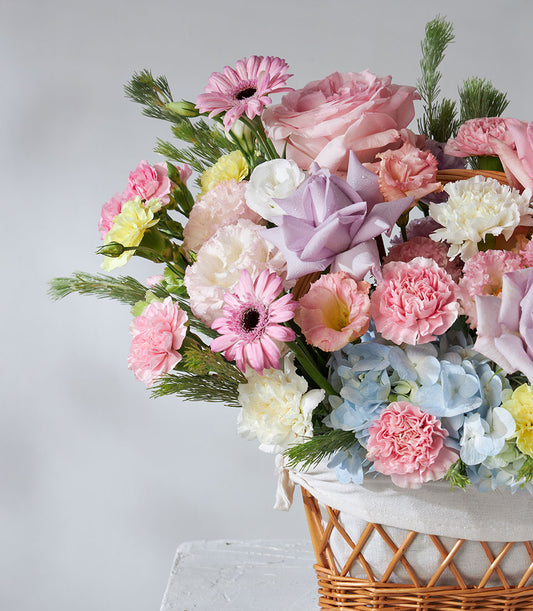 Vibrant pastel flower basket with pink roses, purple roses, gerbera daisies, carnations, hydrangeas and greenery in wicker