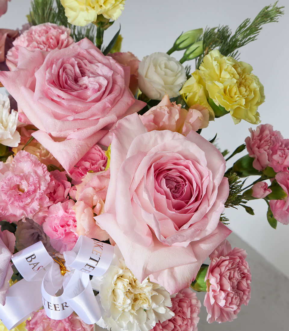 Vibrant pink roses, yellow and white carnations in fresh flower basket with silk ribbon bow