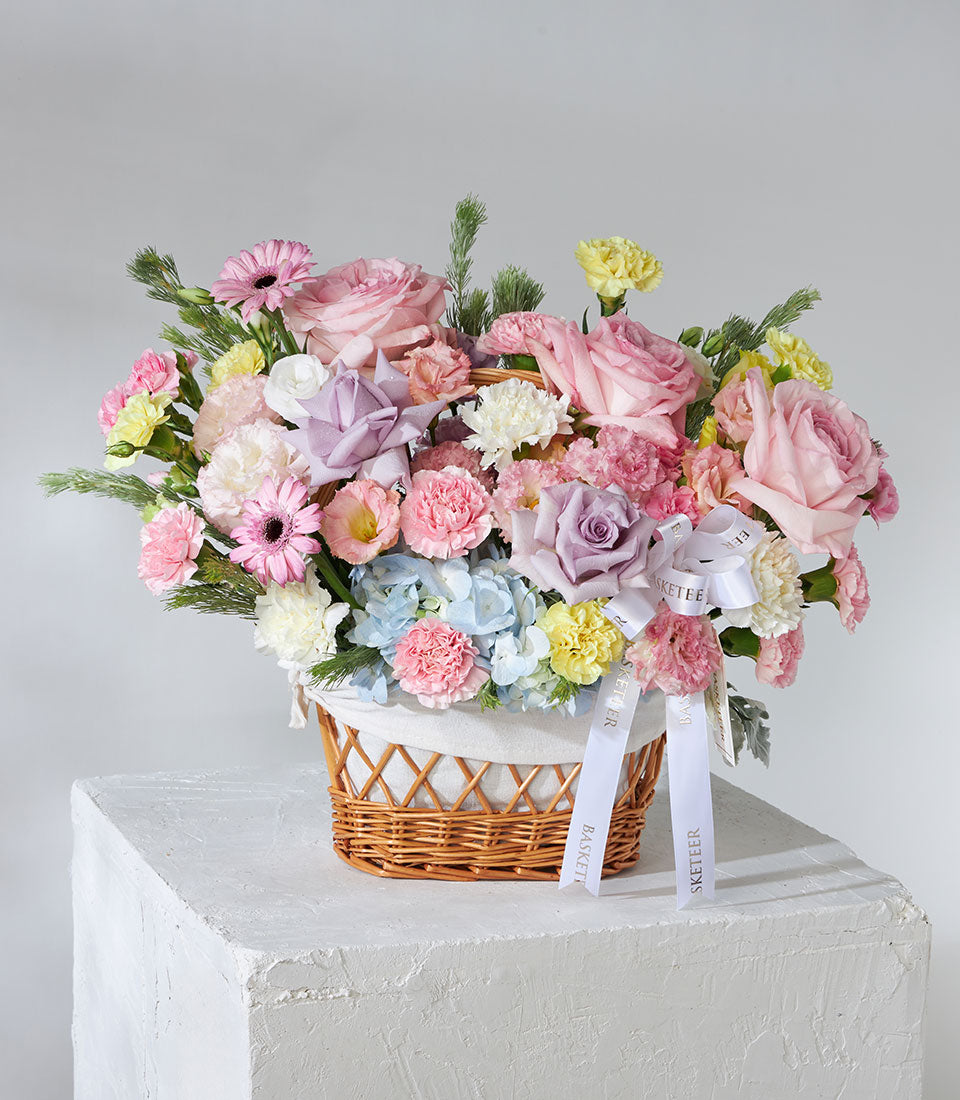 Vibrant pink, purple, yellow, and blue flower basket with roses, carnations, and hydrangeas in woven wicker for birthdays