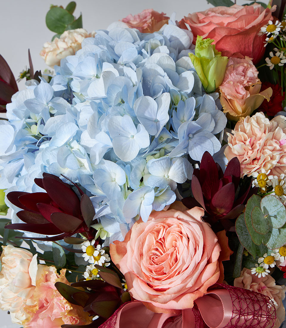 Vibrant fresh flower basket with light blue hydrangeas, peach roses, pink carnations, and white daisies for get well wishes