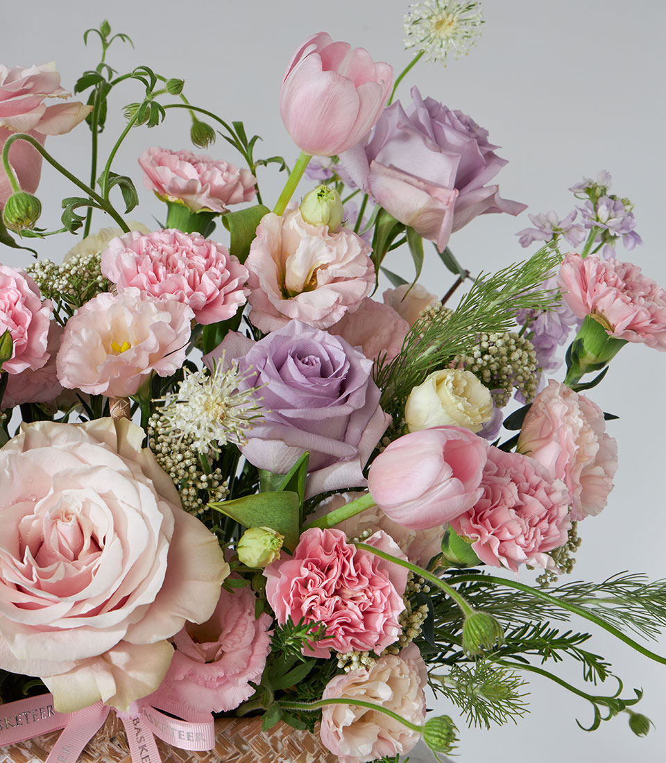 Lavender Bloom flower basket with pink tulips, purple roses, and cream eustoma in woven basket