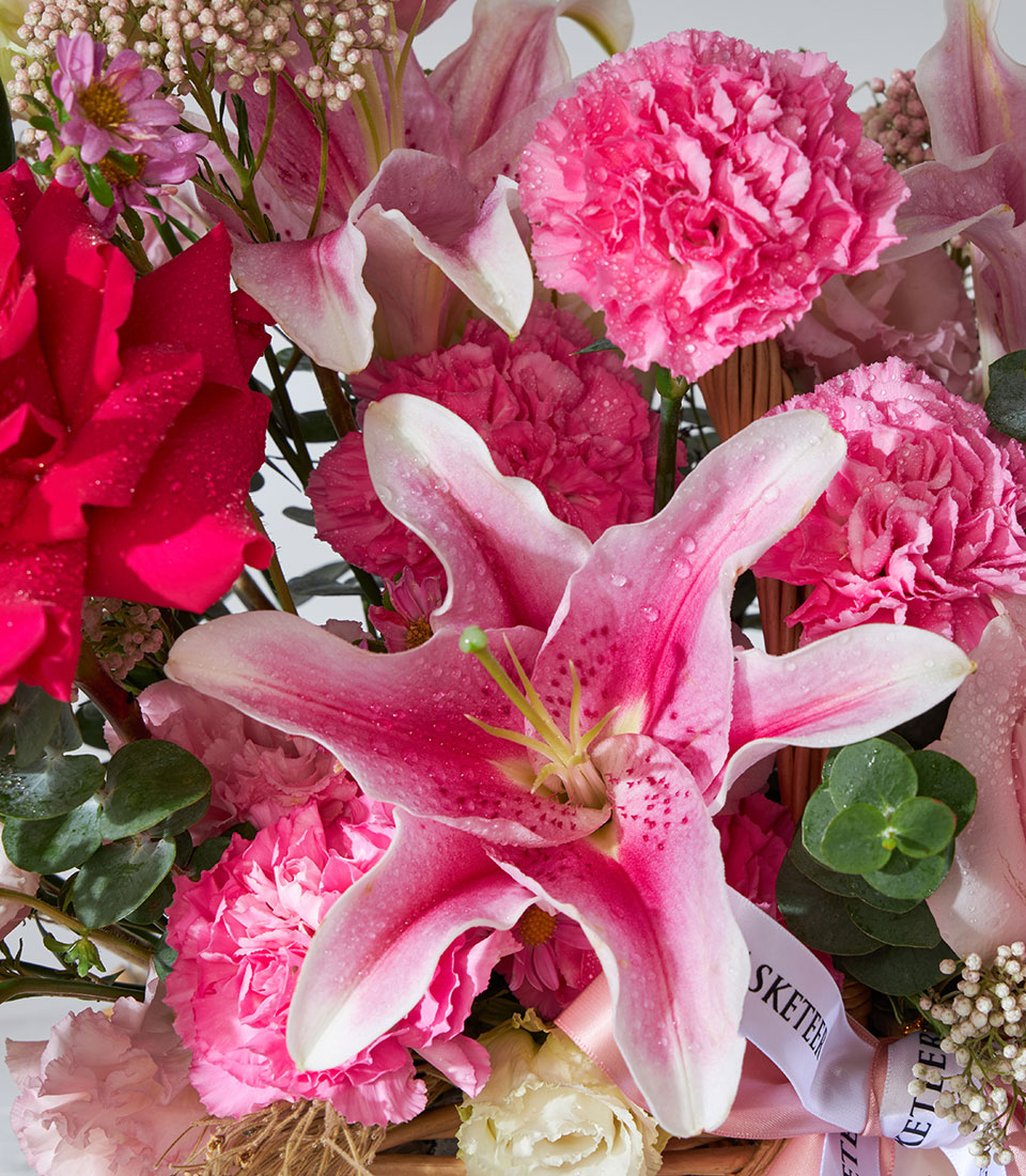 Pink Mondial roses, stargazer lilies, and carnations in a woven basket with eucalyptus, birthday flower gift