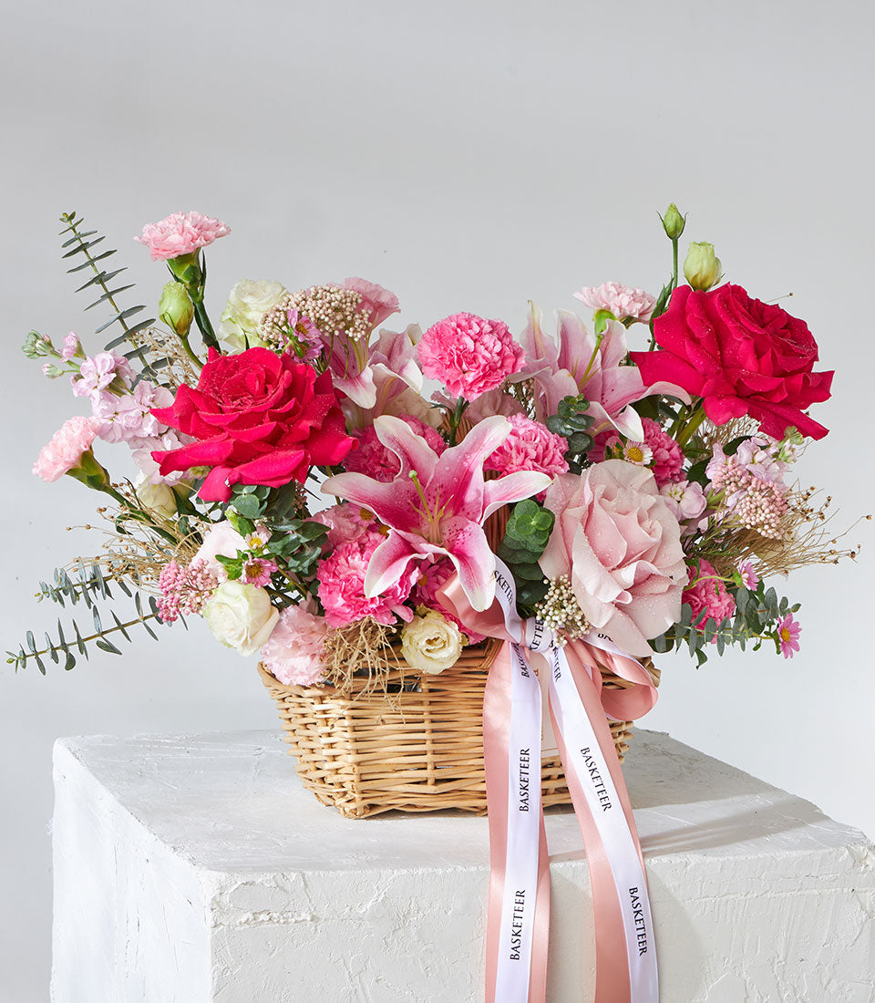 Pink lilies and roses in wicker basket with white ribbon, perfect birthday flower gift