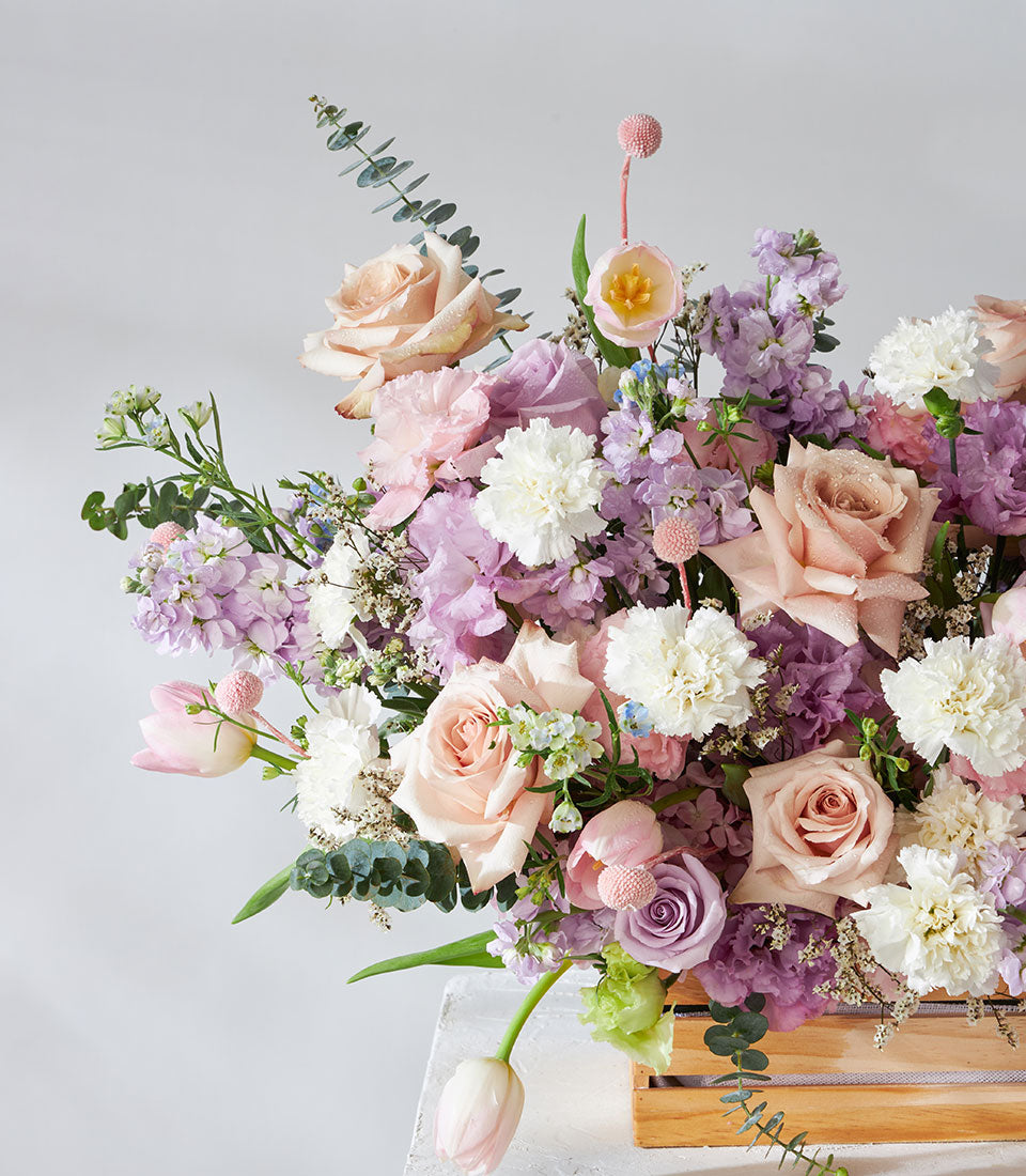 Pastel pink, purple, and white roses with carnations in wooden crate flower arrangement for get well wishes