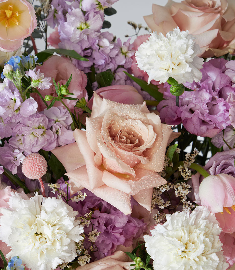 Pastel pink, purple, and white rose and carnation flower arrangement in basket for get well wishes