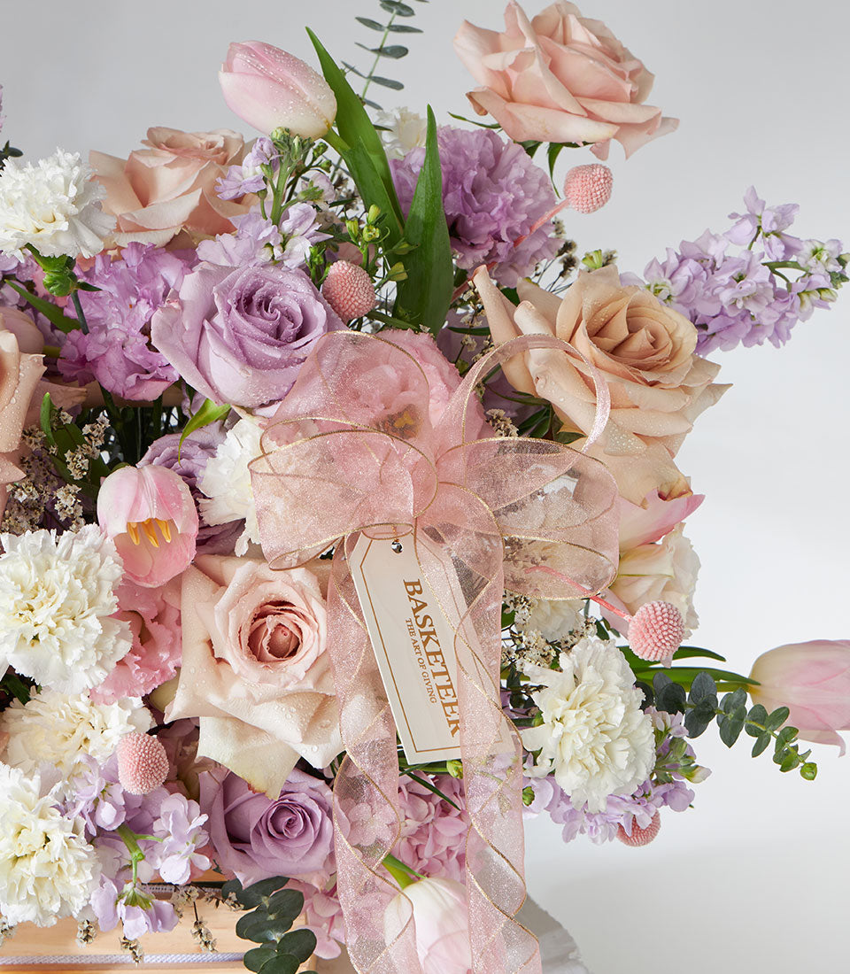 Pastel pink, purple and white rose and tulip arrangement in basket with gold-edged ribbon, get well flowers