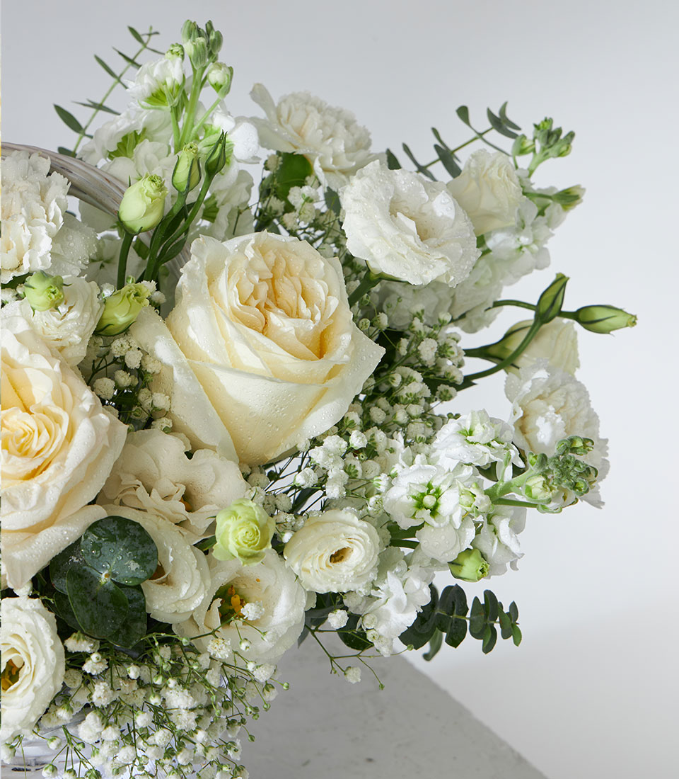 White garden roses, lisianthus, and baby's breath in wicker basket arrangement with fresh water droplets