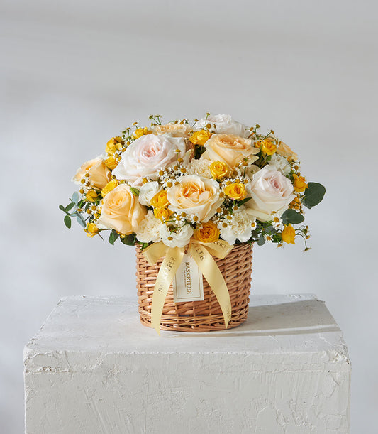 Sunshine Bloom wicker basket with white, pale pink, and yellow roses accented with baby's breath and green foliage